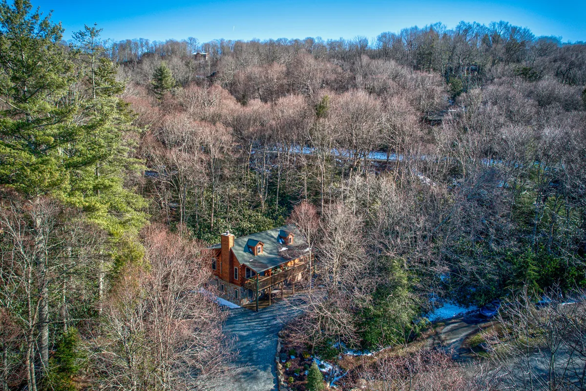 A serene exterior view of the house nestled among mature trees, with a wide driveway leading up to the property. The setting feels private and secluded, surrounded by lush natural landscaping, ideal for peaceful retreats and nature walks.