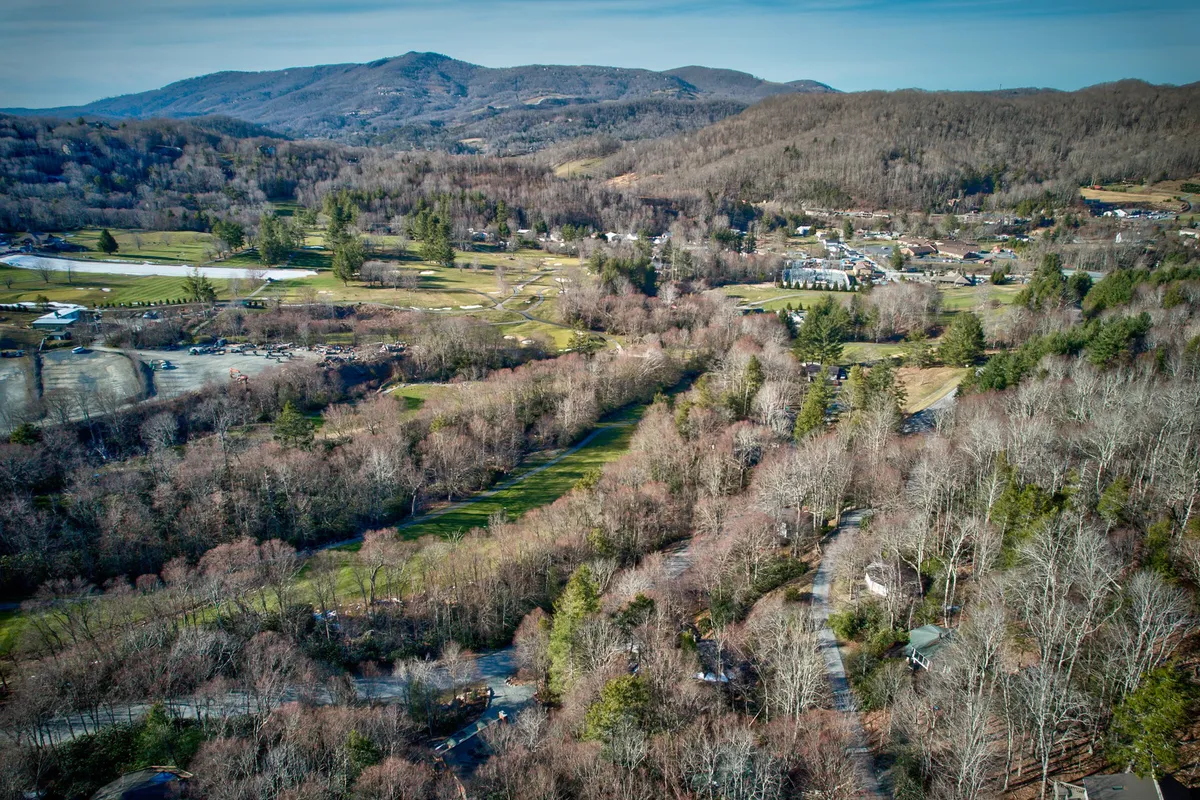 A sweeping view of a mountain range dotted with scattered houses, a golf course, and tree-lined areas. The scene highlights the expansive beauty, recreational opportunities, and proximity to resort amenities.