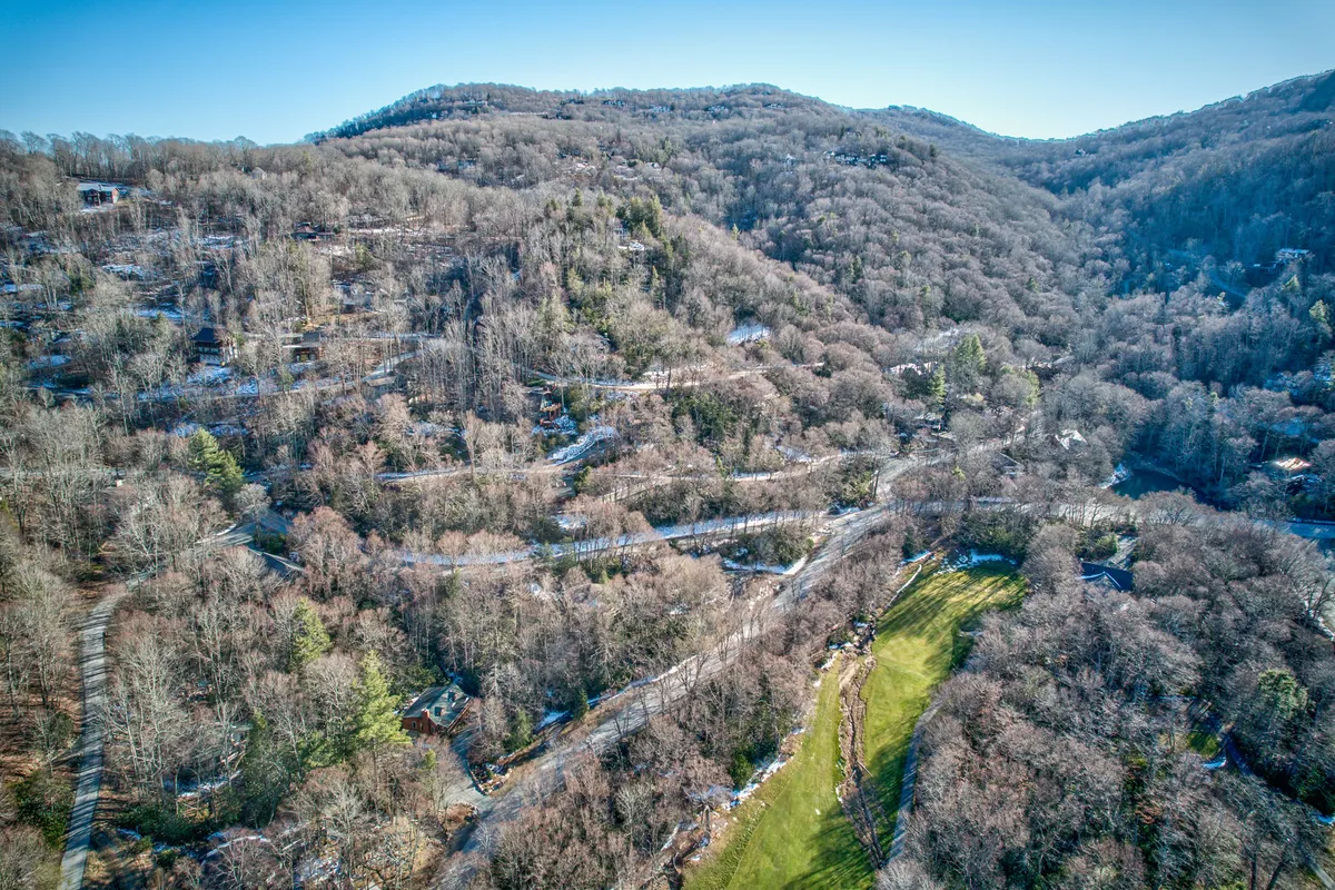 A scenic wide-angle view of rolling hills dotted with houses, expansive green fields, and winding roads. The setting is lush and vibrant, with mountains rising in the background—perfectly capturing the sense of escape and adventure promised in the section.