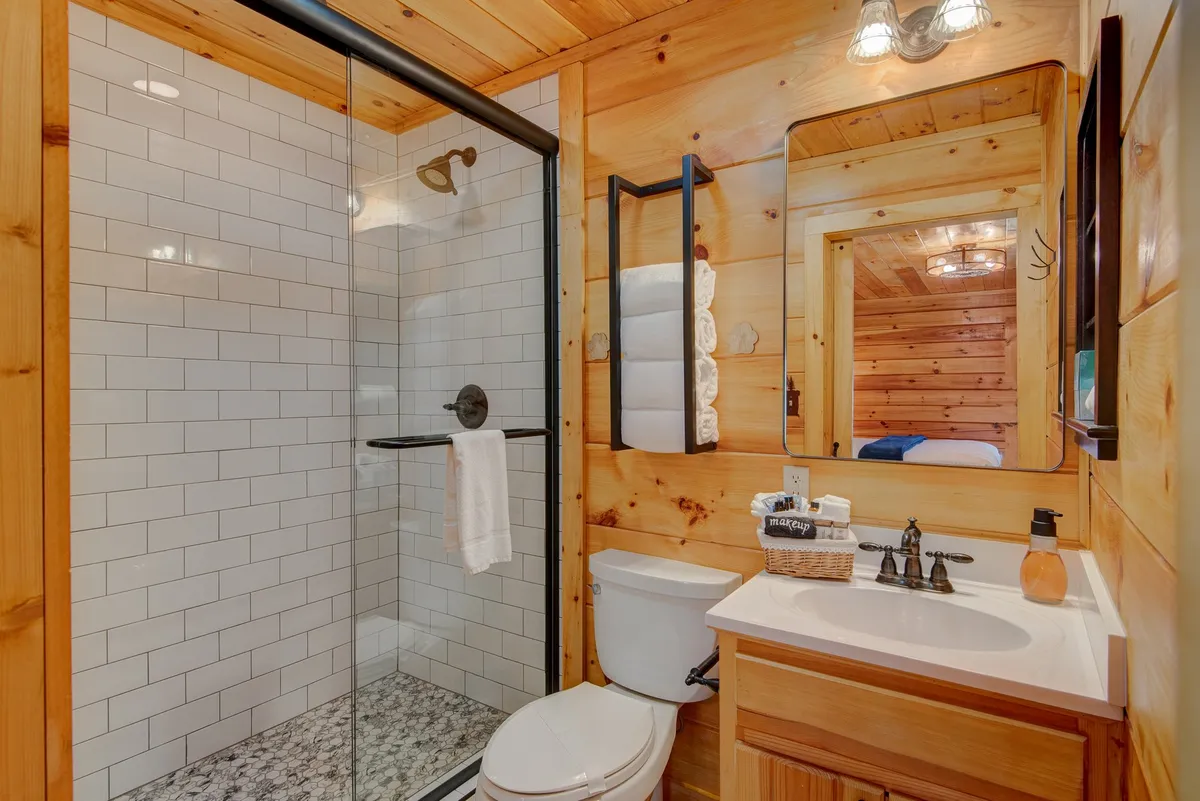 A stylish bathroom showcasing a glass shower enclosure, wooden vanity, black-framed mirror, and decorative towels. Warm lighting and natural textures create an inviting, spa-like environment.