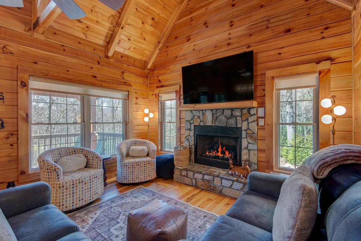 A warm, inviting living space with a fireplace, expansive windows bringing in natural light, and comfortable seating arranged for relaxation or socializing. Textured walls add character, and the setup suggests a space ideal for unwinding or gathering with friends or family.