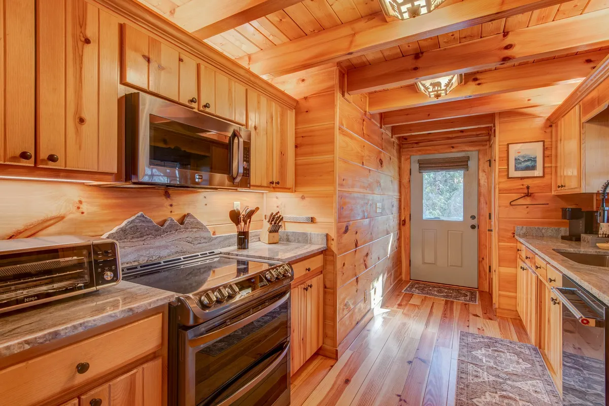 A modern, functional kitchen with stainless steel appliances, granite countertops, and warm wooden cabinetry, opening up to the rest of the house. The kitchen is well-lit and ready for shared cooking adventures and family gatherings.